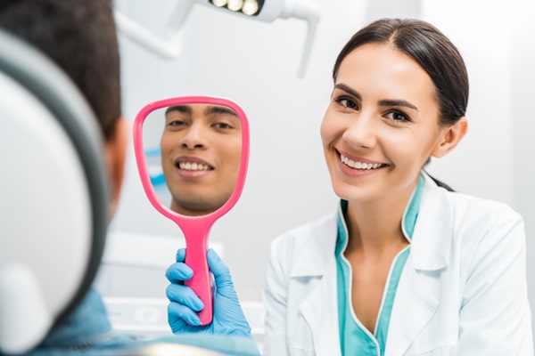 handsome african american man smiling while female dentist holding mirror
