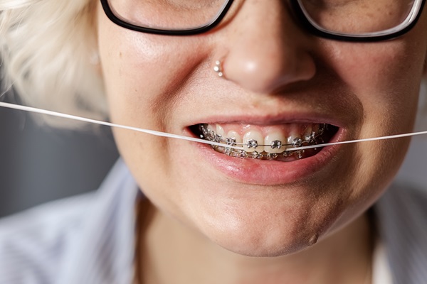 a young woman with braces brushes her teeth with dental floss