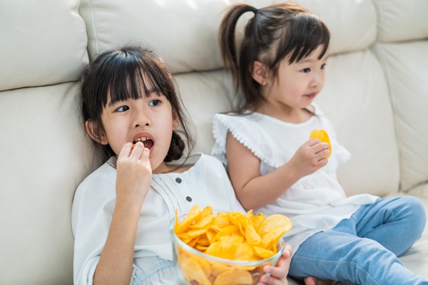 two asian kids eating potato chips in the couch