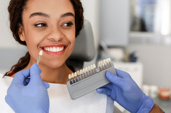 Dentist in blue medical gloves applying sample from tooth enamel scale to happy black woman patient teeth, close up