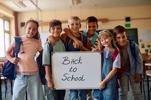 Happy elementary students holding back to school sign in the classroom and looking at camera.