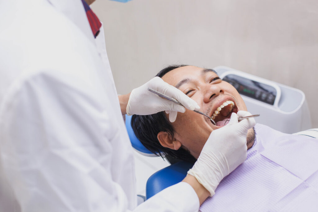 Dentist wearing gloves examining a smiling male patient's teeth with a dental mirror and probe during a routine check-up