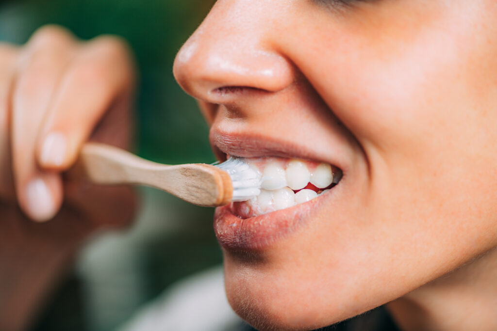 Close-up of a woman brushing her teeth with a bamboo toothbrush, part of a daily oral care routine that can include oil pulling